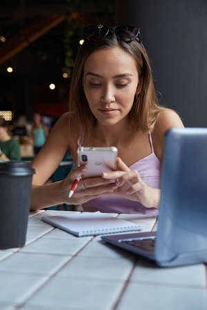 young well dressed asian woman sitting at table, using her smartphone. beautiful lady surfing...