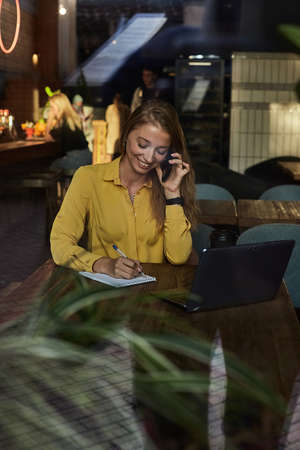 young caucasian pretty woman sitting at table of coffee shop, calling by smartphone. beautiful...