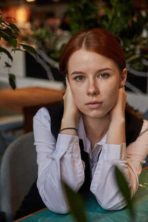 young caucasian stylish redhead pretty woman with long hair sitting at coffee shop table, wrapping...