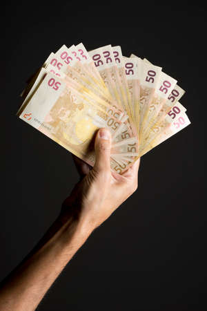 Human hand holding money - fifty euro banknotes isolated on a dark gray background