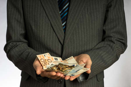 Businessman hand holding money, euro bills. Banknotes isolated gray background. Hand holding out a stack of fifty eurosの写真素材