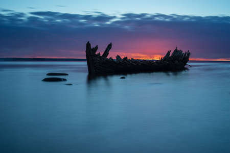 Old broken boat wreck on the shore, a frozen sea and beautiful blue sunset background. Estonia, Europe.の写真素材