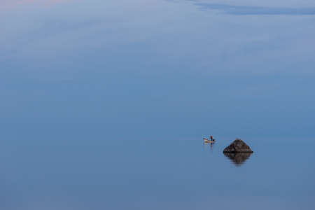 Boat, fisherman and sunlight on the coast. Man fishing in evening, blue sky reflection on water. Beach in summer. Seaside natural environment. Shore in island, Nature Reserve in Estonia, Europeの写真素材