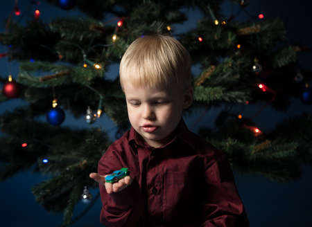 Kid and multicolor spruce with decorations and lights bokeh. Little boy and toy car under the multicoloured Christmas treeの写真素材
