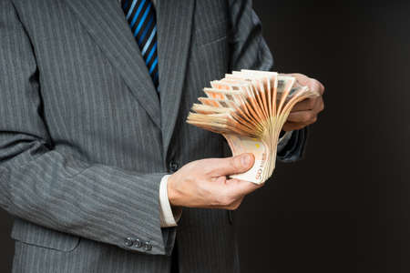 Business man is holding cash, fan of fifty euros. Person counts money. Businessman hands and euro bills, isolated gray background.の写真素材