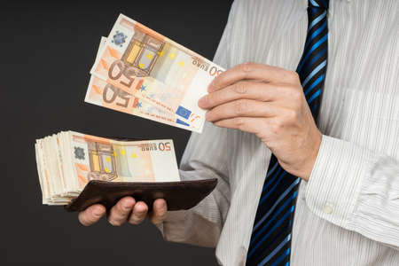 Businessman putting banknotes in his wallet.   Stack of fifty euros money. Business man is holding...
