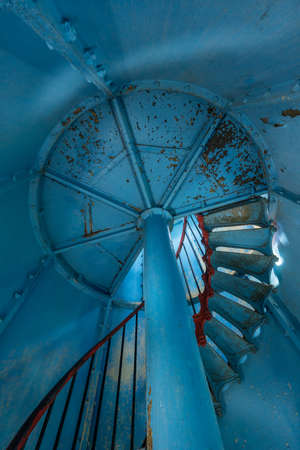 Old lighthouse on the inside. Red iron spiral stairs, round window and blue wall. Kihnu, small island in Estonia. Europeの写真素材