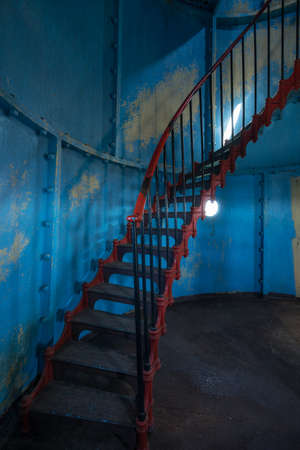 Old lighthouse on the inside. Red iron spiral stairs, round window and blue wall. Kihnu, small island in Estonia. Europeの写真素材