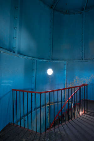 Old lighthouse on the inside. Red iron spiral stairs, round window and blue wall. Kihnu, small island in Estonia. Europeの写真素材