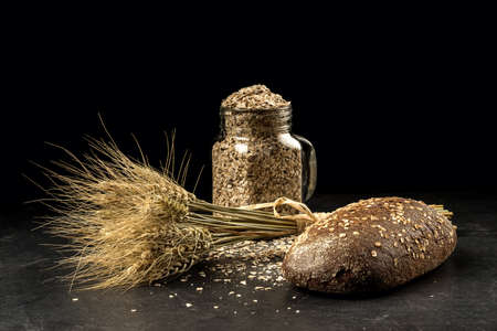 Grain bouquet, golden oats spikelets in jar on dark wooden table, buns and can filled with dried...
