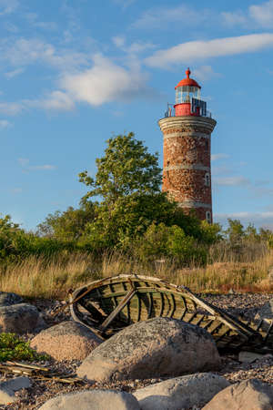Lighthouse and old boat in the Baltic Sea. Shore, evening light, sunset, clouds and architecture concept. Mohni, small island in Estonia, Europe.の写真素材