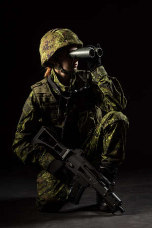 Portrait of armed woman with camouflage. Young female soldier observe with binoculars. Child soldier with gun in war, hause ruins background.  Military, army people conceptの写真素材