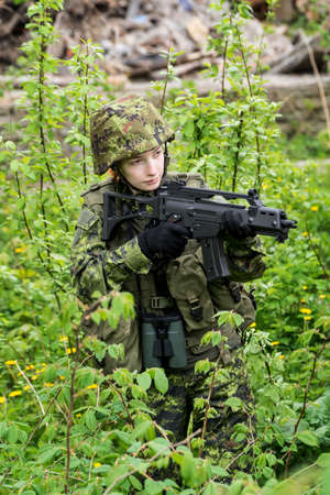 Portrait of armed woman with camouflage. Young female soldier observe with firearm. Child soldier...