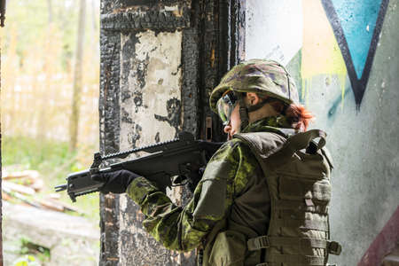 Portrait of armed woman with camouflage. Young female soldier observe with firearm. Child soldier with gun in war hearth, house ruins background.  Military, army people conceptの写真素材
