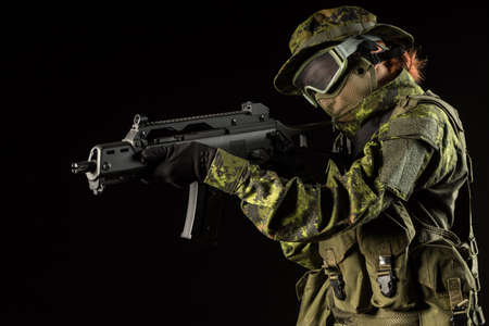 Portrait of armed woman with camouflage. Young female airsoft sniper observe with firearm. Soldier with gun in war, black background.  Military, army people conceptの写真素材