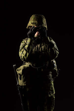 Portrait of armed woman with camouflage. Young female soldier observe with binoculars. Child soldier with gun in war, black background.  Military, army people conceptの写真素材
