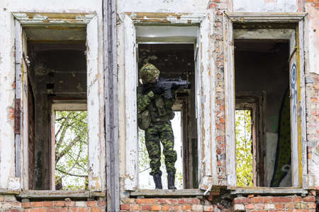 Portrait of armed woman with camouflage. Young female soldier observe with firearm. Child soldier with gun in war hearth, house ruins background.  Military, army people conceptの写真素材