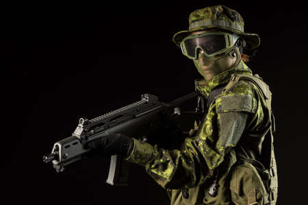 Portrait of armed woman with camouflage. Young female airsoft sniper observe with firearm. Soldier...