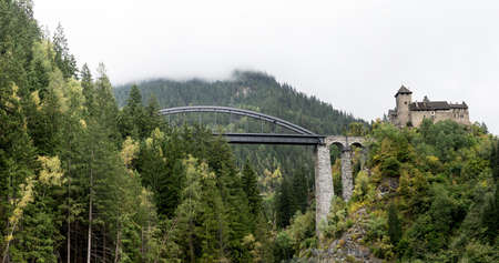 Schloss Wiesberg Castle with bridge over the Trisanna river. Mountain, colored hills and trees landscape natural environment on background. Paznautal Valley, Paznaun, Tyrol, Austria.のeditorial素材