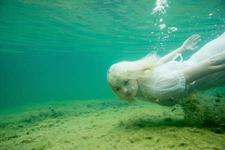 A floating woman. Underwater portrait. Girl in white dress swimming in the lake. Green marine plants and waterの写真素材