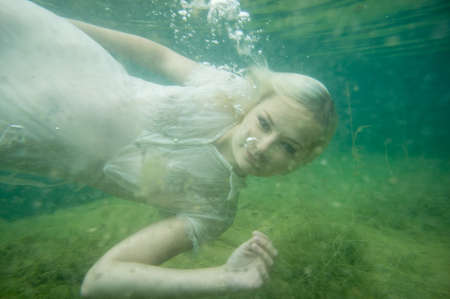 A floating woman. Underwater portrait. Girl in white dress swimming in the lake. Green marine plants and waterの写真素材
