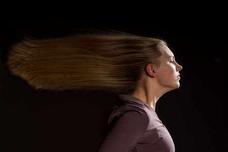 Caucasian white female model portrait. The wind blowing the long blonde hair off on beautiful girl. Woman posing studio shot on a black backgroundの写真素材