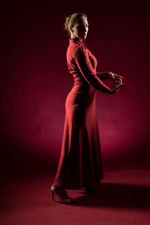 Lady in red gown standing and posing  in studio. Portrait of beautiful elegant woman in evening dressの写真素材
