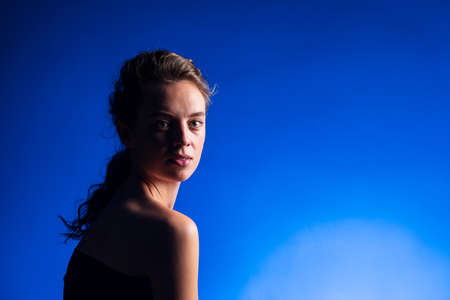 Beautiful woman with brunette long curly hair. Beauty portrait of modern fashion, blue background.の写真素材