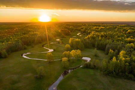 Forest in summer colors. Green deciduous trees and winding blue river in sunset. Mulgi meadow,...