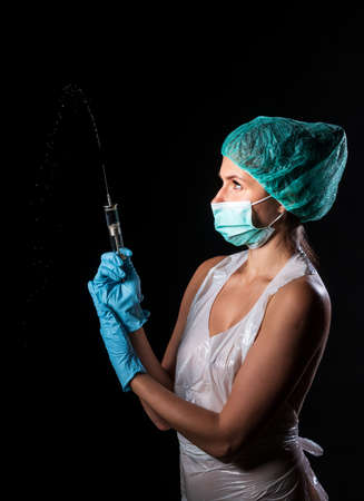 Sexy doctor in medical mask make protective injection. Naked nurse prepares syringe. Medic in disposable medical clothing. preparing vaccination against for a pandemic and flu season.の写真素材