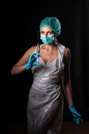 Sexy doctor in medical mask make protective injection. Naked nurse prepares syringe. Medic in disposable medical clothing. preparing vaccination against for a pandemic and flu season.の写真素材