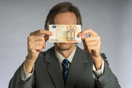Businessman hand holding money, euro bill. Hands holding fifty euros in front of faceの写真素材