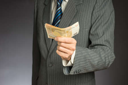 Businessman hand holding money, euro bills. Banknotes isolated gray background. Hand holding out a stack of fifty eurosの写真素材
