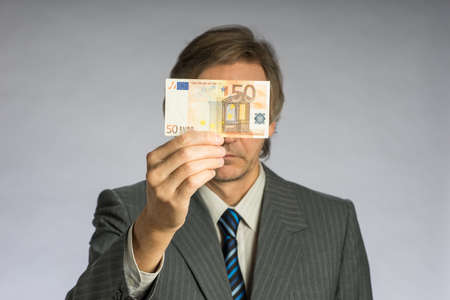 Businessman hand holding money, euro bill. Hands holding fifty euros in front of faceの写真素材