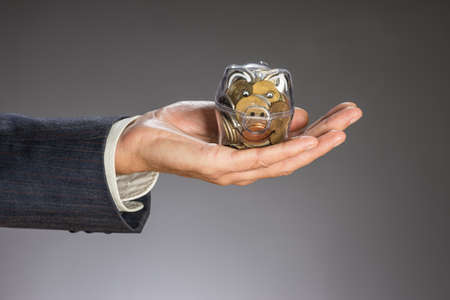 Business man with gray jacket putting euro coin  into the  piggi bank. European finance currency. Guy holding money boxの写真素材