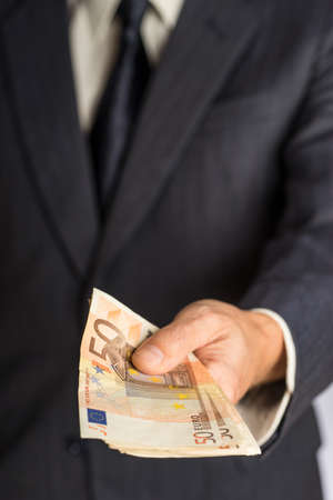 Businessman hand holding money, euro bills. Banknotes isolated gray background. Hand holding out a stack of fifty eurosの写真素材