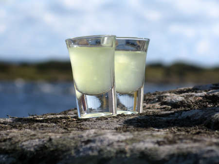 Two shot glasses of limoncello on a rock by the ocean の写真素材