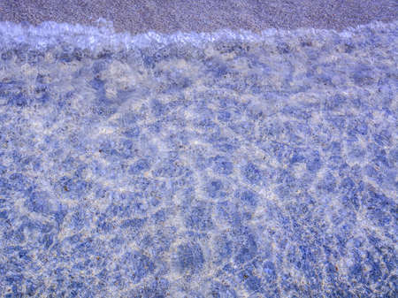Shallow transparent water surface with small seashells and rocks as abstract background の写真素材