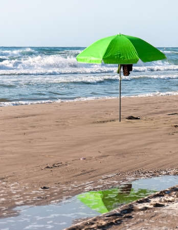 Green umbrella with reflection in pool of water on a beach の写真素材