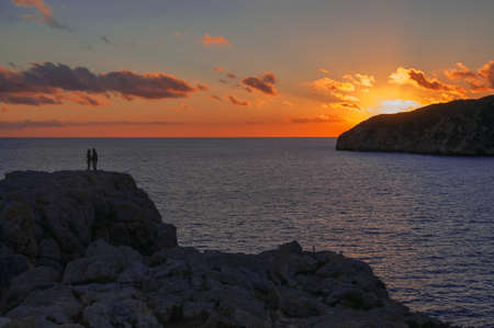 Romantic couple on a rock by the Mediterranean ocean at a sunset in February の写真素材