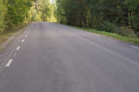 Empty asphalted country road approaching a hill, through a forest in Sormland, Sweden 