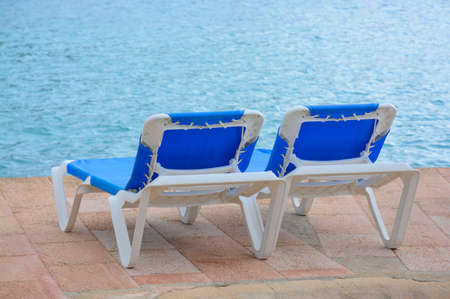 Two empty blue lounge chairs by the ocean 