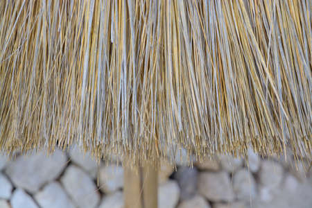 Straw parasol detail on sandy beach with dry wall in the background の写真素材