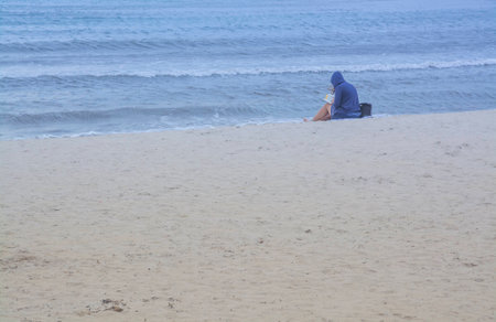 Beach reading  Young woman sitting on a sandy and empty beach reading a book  Mallorca, Balearic islands, Spain の写真素材