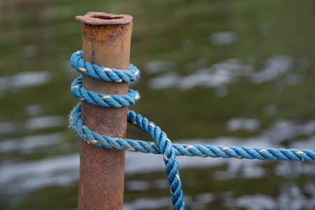 Blue boating knot rope tied around rusty pole by the water の写真素材
