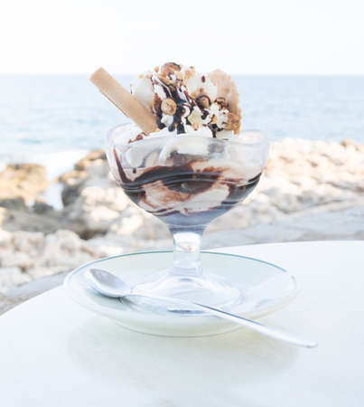 Vanilla icecream in a bowl with hazelnuts, chocolate sauce and spoon の写真素材