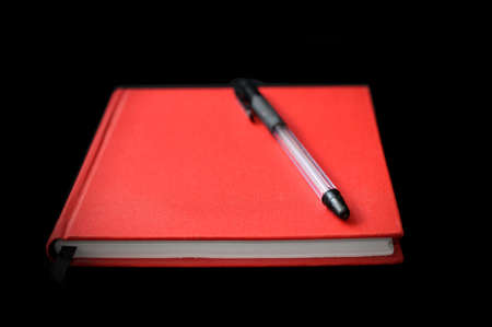 Red notebook with black pen on black background.の写真素材