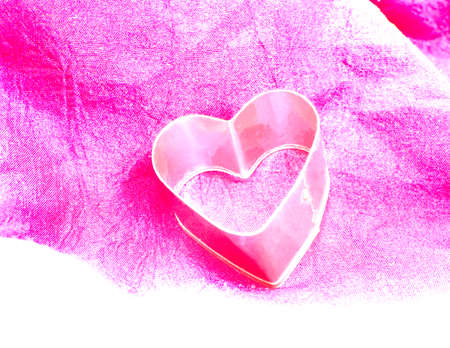 Pink heart. Pink baking tin in the shape of a heart on pink fabric. Filtered and monochrome.の写真素材
