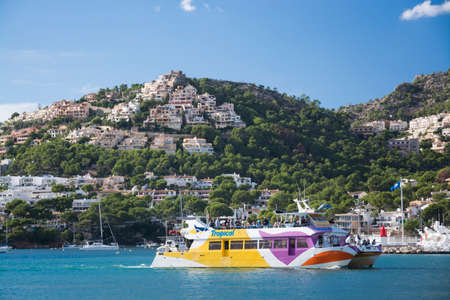 Tourist glass bottom boat and homes perching on the hills above Port Andratx marina. Mallorca,...