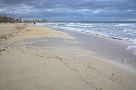 PLAYA DE PALMA, MAJORCA, SPAIN - NOVEMBER 5, 2013:  Man walking with football on the sandy beach with storm waves on November 5, 2013 in Mallorca, Balearic islands, Spain.のeditorial素材